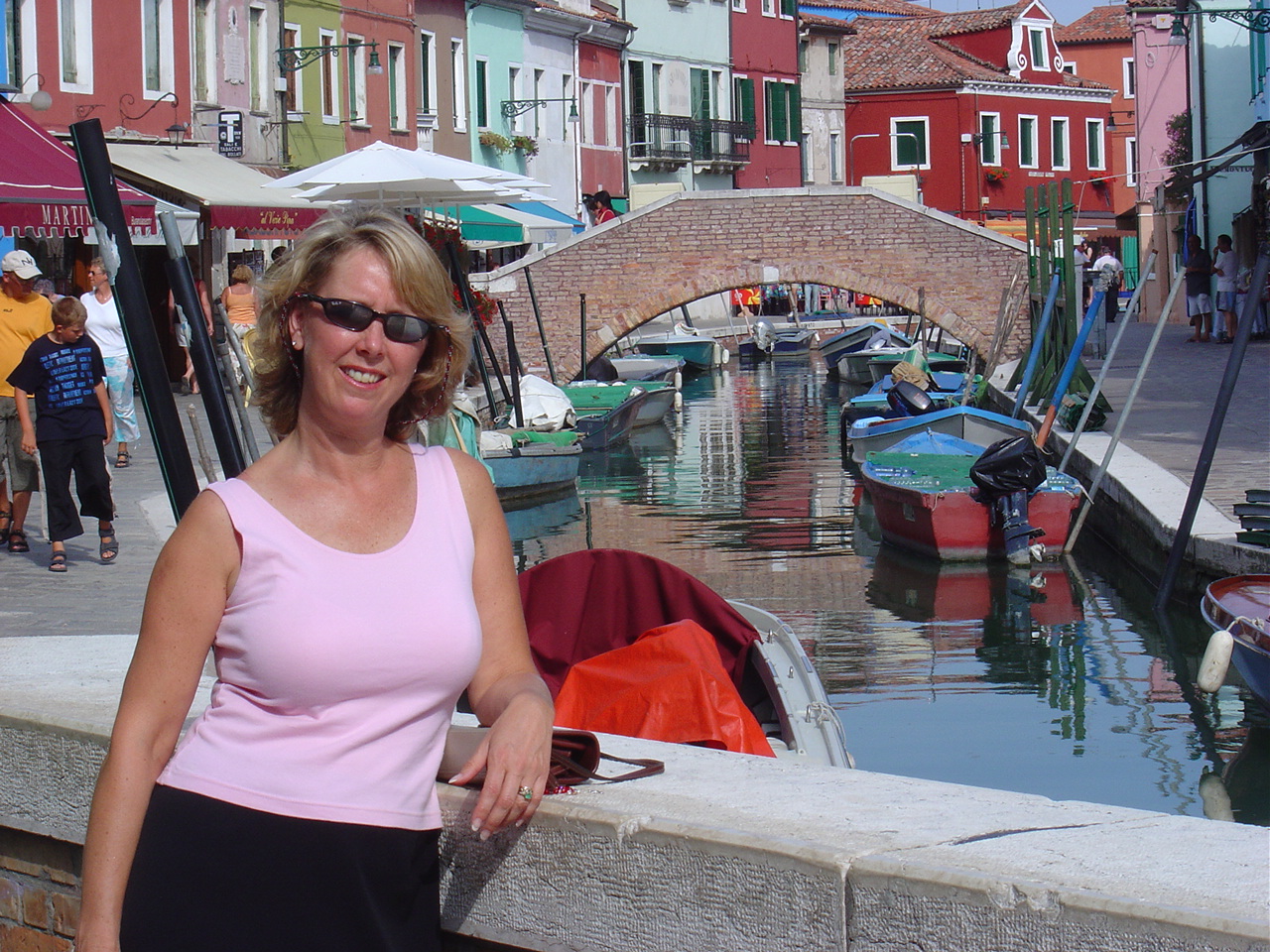 woman in pink shirt standing on canal bridge in burano italy